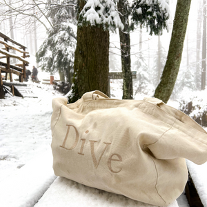 "Dive tote bag resting on a wooden table, surrounded by snow in a serene forest setting."